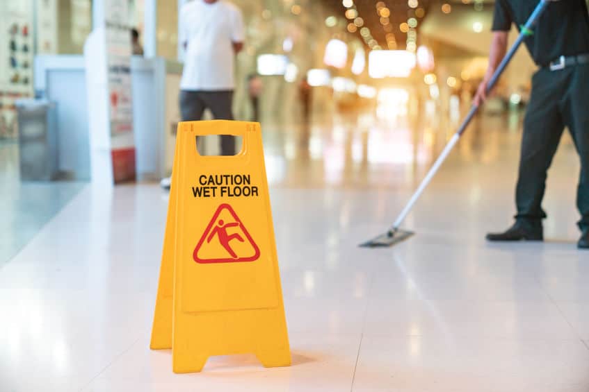 Low Section Of Worker Mopping Floor With Wet Floor Caution Sign Low Section Of Worker Mopping Floor With Wet Floor Caution Sign
